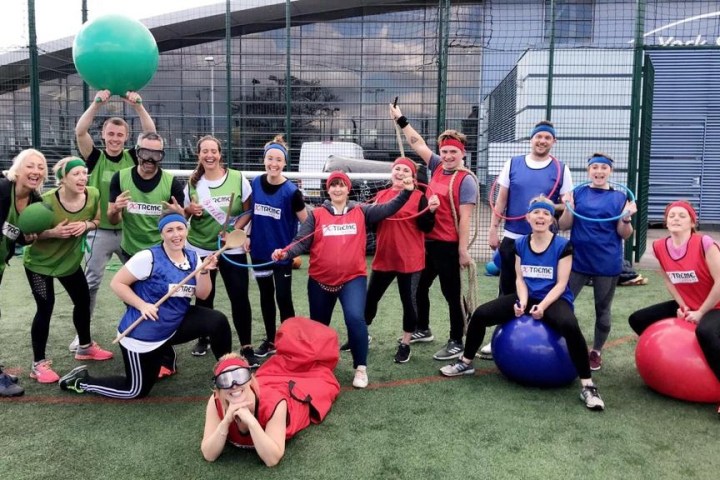 Group of people in sports attire posing with exercise balls and ropes on an outdoor field.