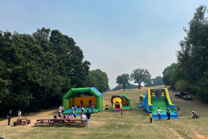 Outdoor field with bounce house, inflatable slides, and people standing nearby.