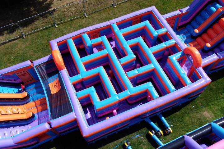 Colorful inflatable maze and slides on grass, viewed from above.