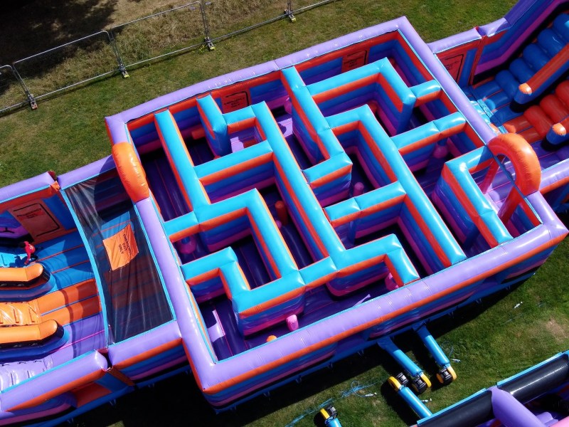 Colorful inflatable maze and slides on grass, viewed from above.