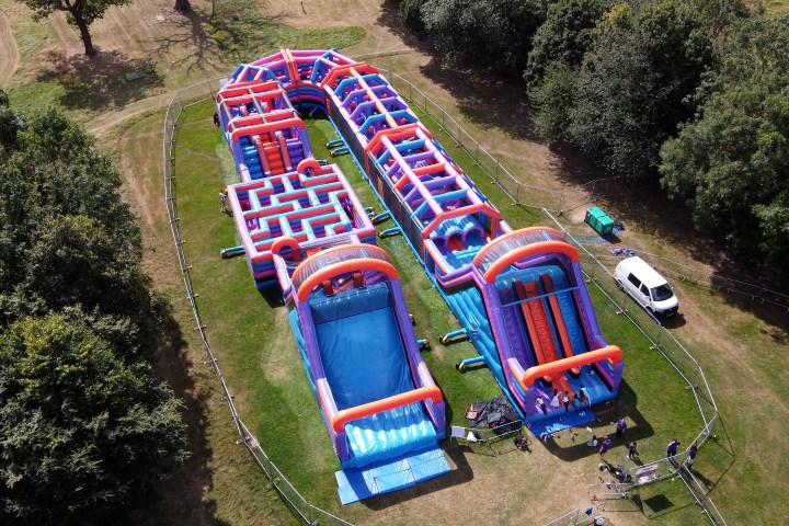 Aerial view of an inflatable obstacle course on a grassy field with trees.