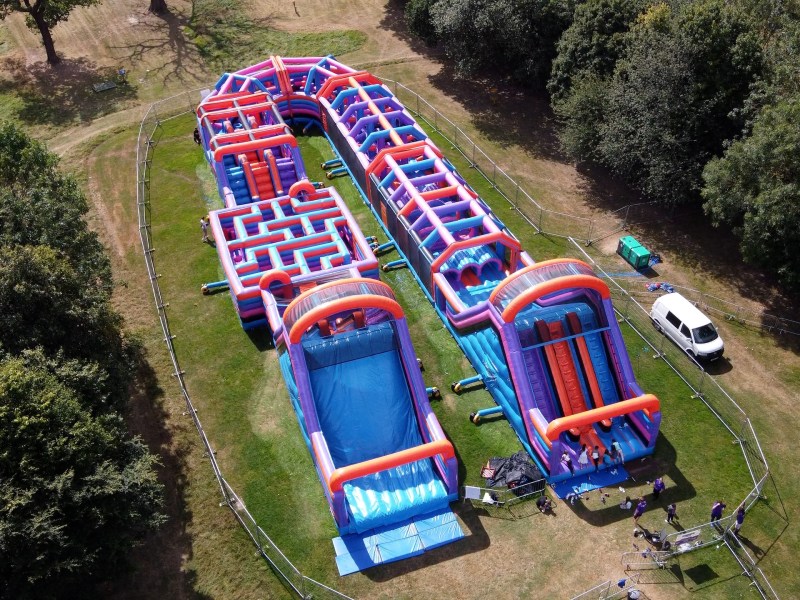 Aerial view of an inflatable obstacle course on a grassy field with trees.
