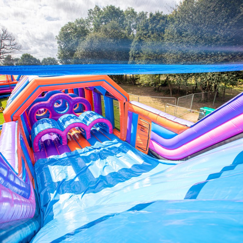 Colorful inflatable obstacle course with slides and arches in an outdoor setting.
