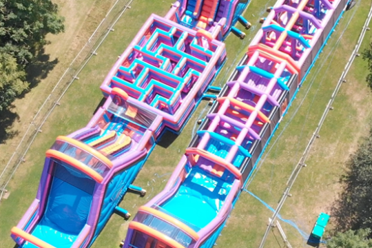 Aerial view of large, colorful inflatable obstacle courses on grass.