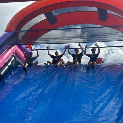 Four people seated atop a large inflatable slide with arms raised.