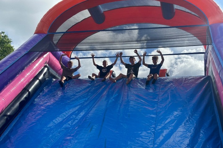 Four people seated atop a large inflatable slide with arms raised.
