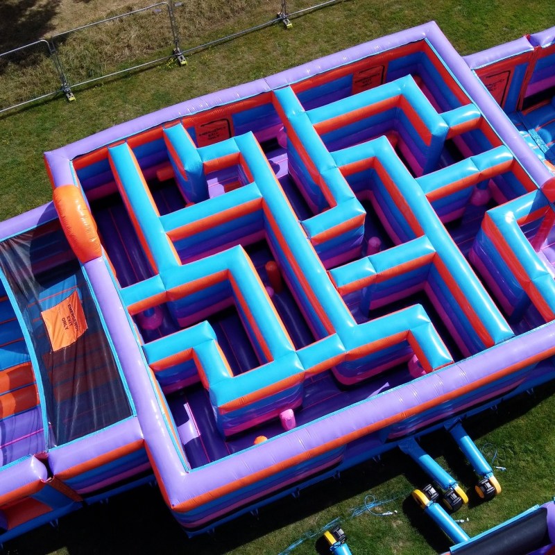 Colorful inflatable maze and slides viewed from above, set on grassy area.