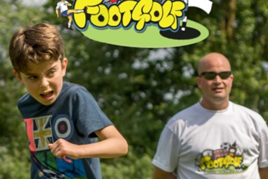 Boy playing footgolf with a man in the background wearing a footgolf t-shirt.