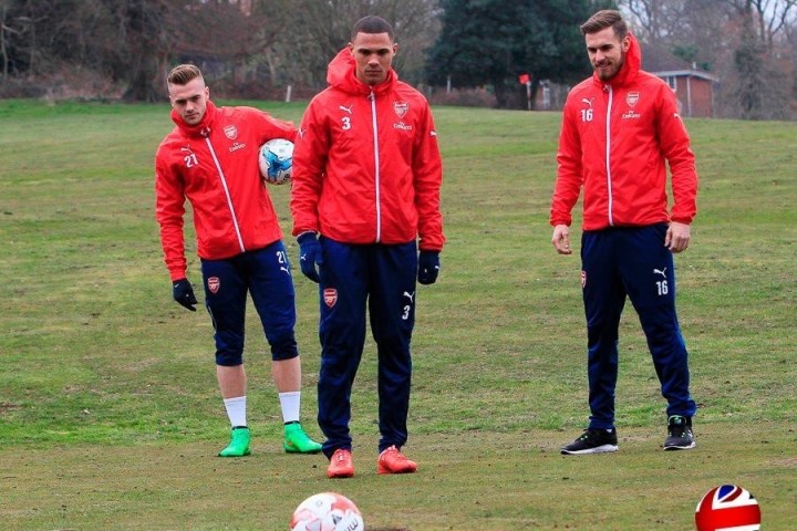 Three people in red jackets playing footgolf on a grassy field.