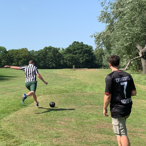 Two people playing soccer in a park; one is kicking the ball.