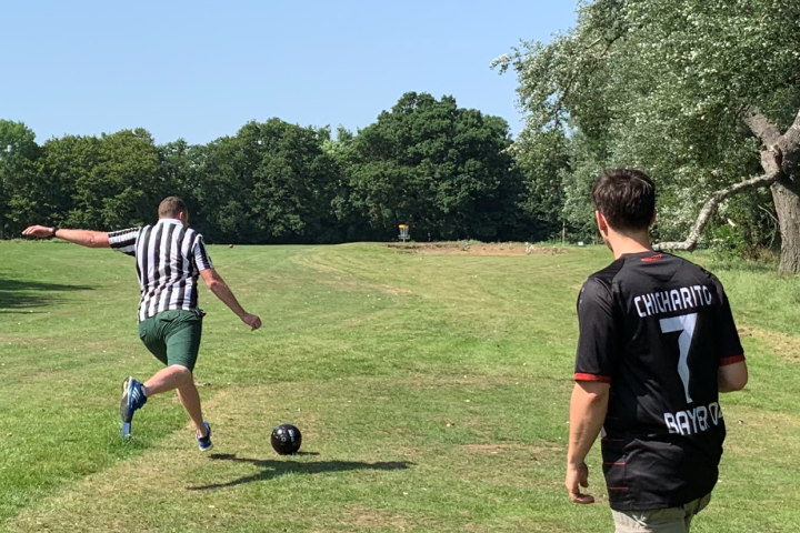 Two people playing soccer in a park; one is kicking the ball.