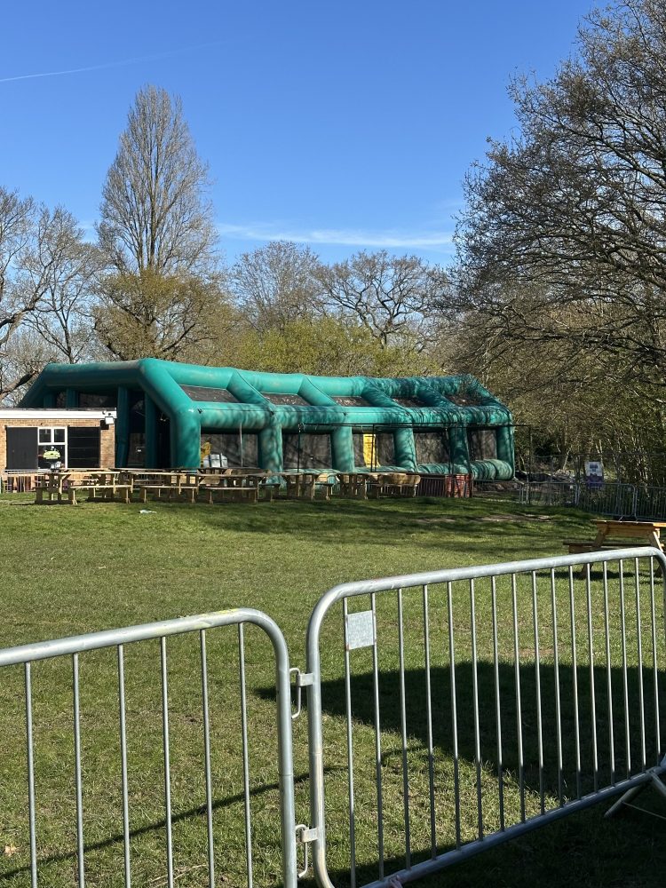 Inflatable structure in a park with trees and a metal barricade.