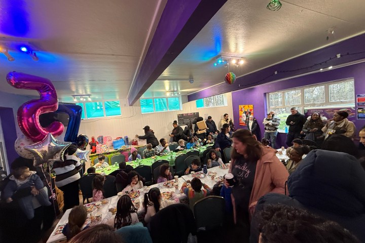 Crowded indoor celebration with balloons and people at decorated tables.