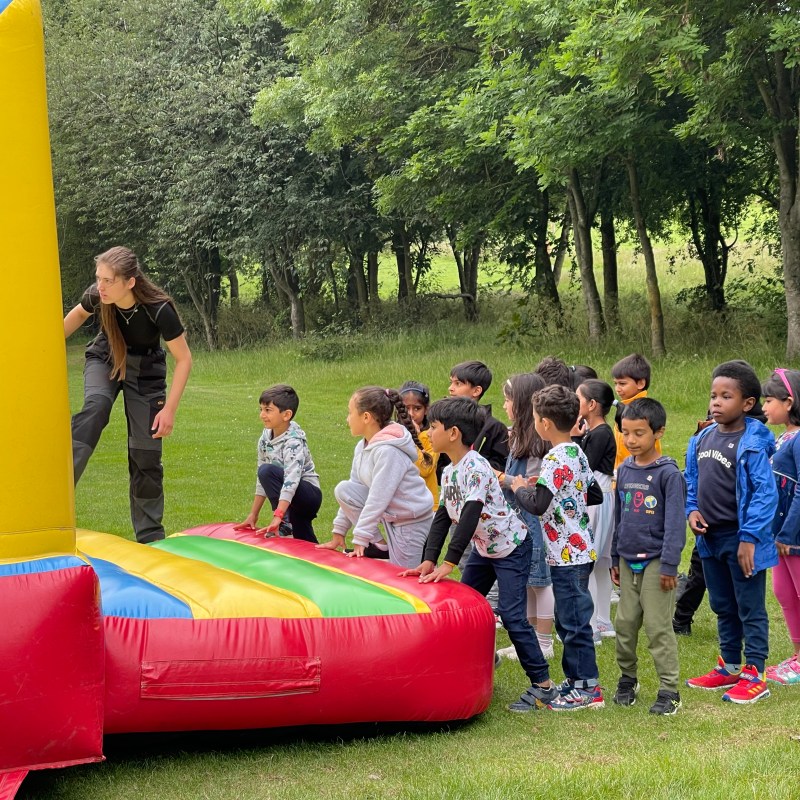 Children lined up for an inflatable slide outdoors with trees in the background.