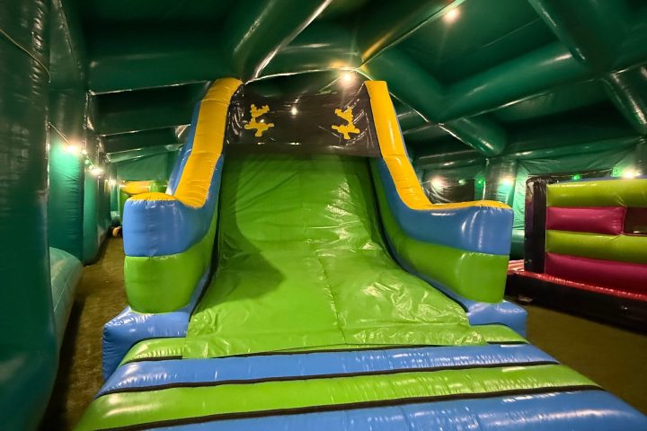 Inflatable slide with green and blue colors inside an indoor play area.