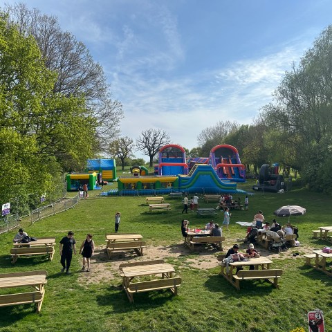 Park with picnic tables and inflatable obstacle course on a sunny day.