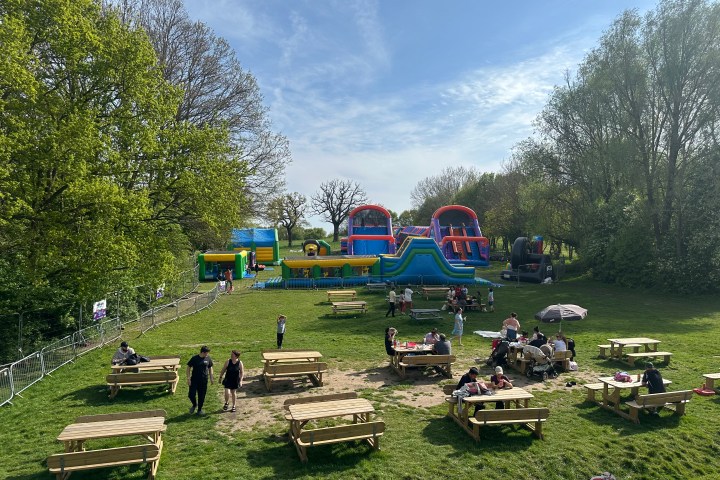 Park with picnic tables and inflatable obstacle course on a sunny day.
