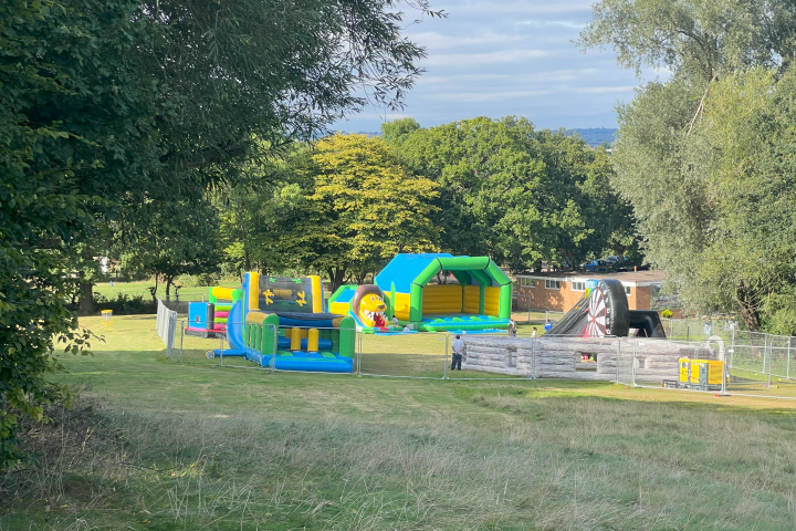 Inflatable obstacle course and slide in a grassy park setting.