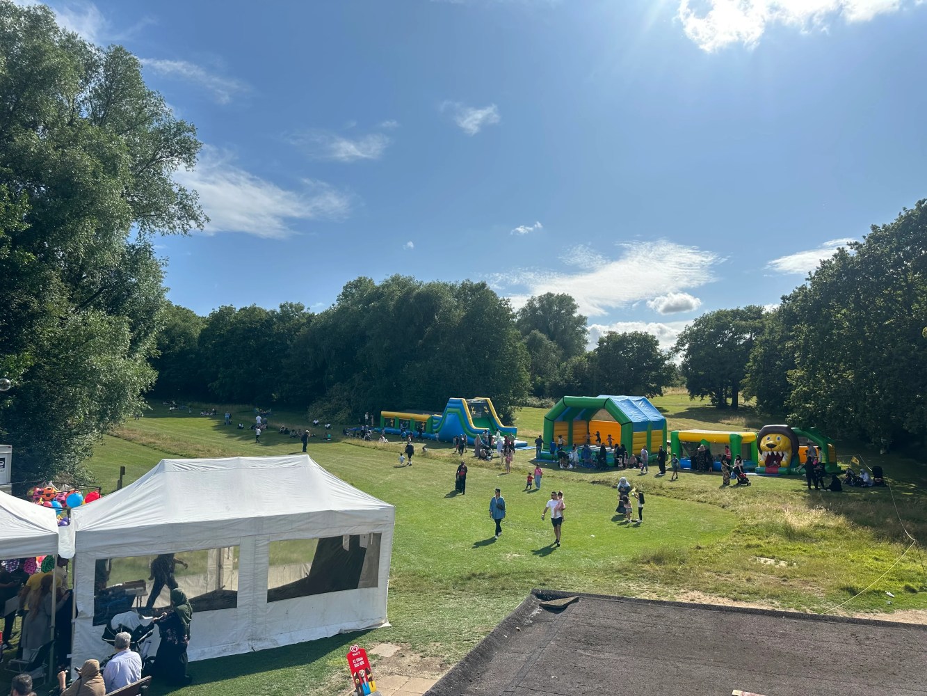 Outdoor fair with bouncy castles and people on grassy field under a sunny sky.