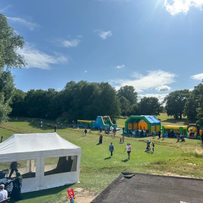 Outdoor fair with bouncy castles and people on grassy field under a sunny sky.
