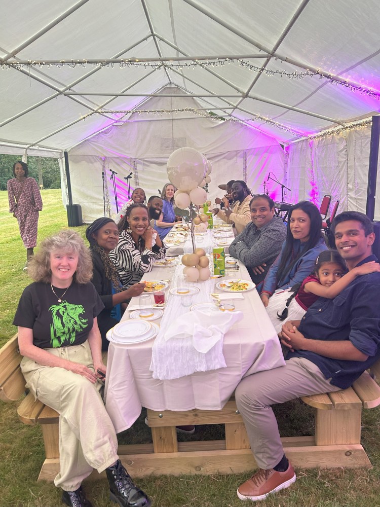 People seated at a long table in a tent with white decor and pink lighting.