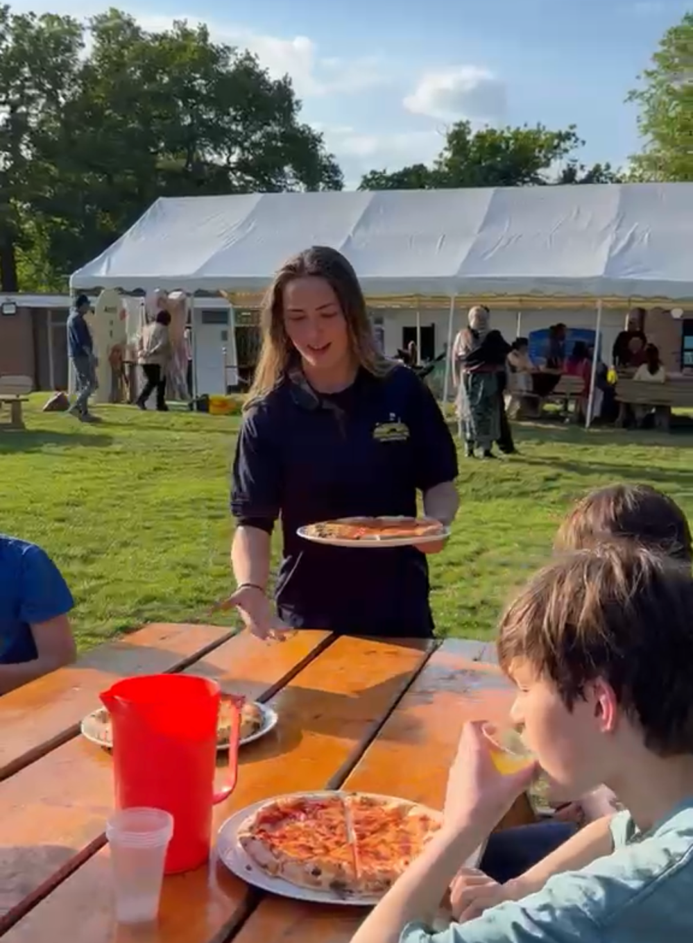 People enjoying pizza at an outdoor picnic with a tent in the background.