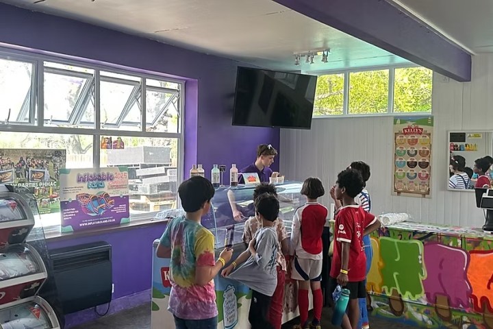 Kids in a colorful ice cream shop with purple walls, ordering from a counter.