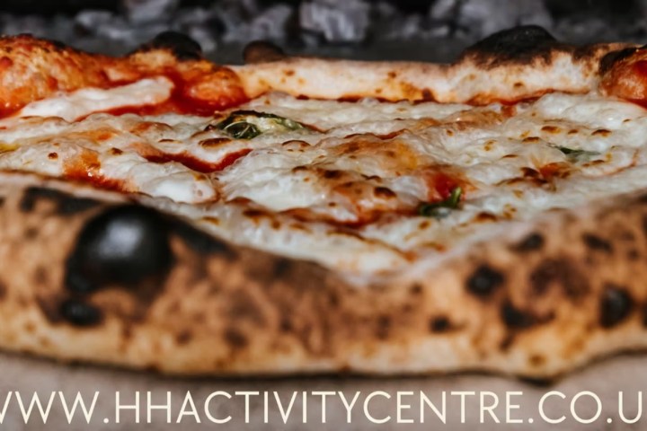 Wood-fired pizza with melted cheese and tomato sauce in an oven.