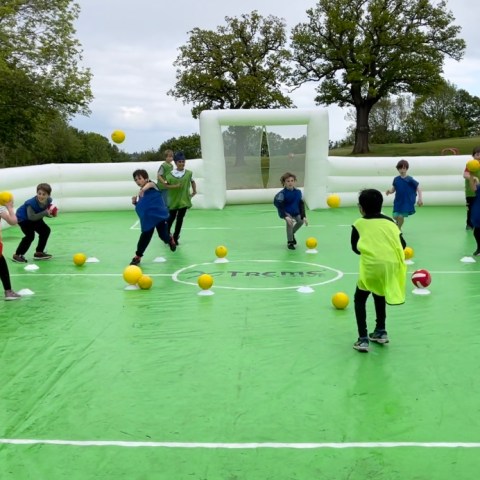 Children playing a ball game on a green inflatable field.